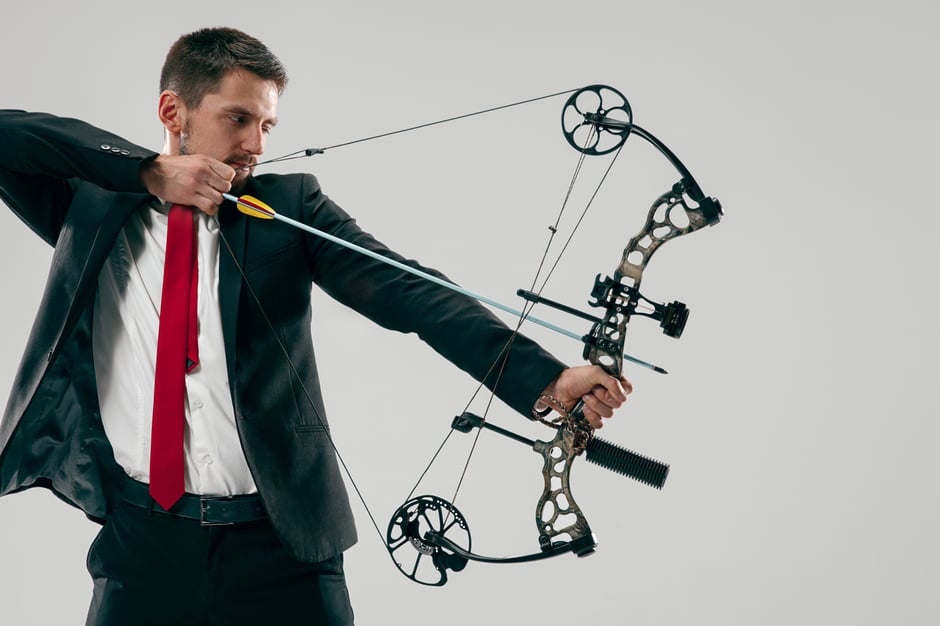 businessman-aiming-at-target-with-bow-and-arrow-isolated-on-gray-studio-wall